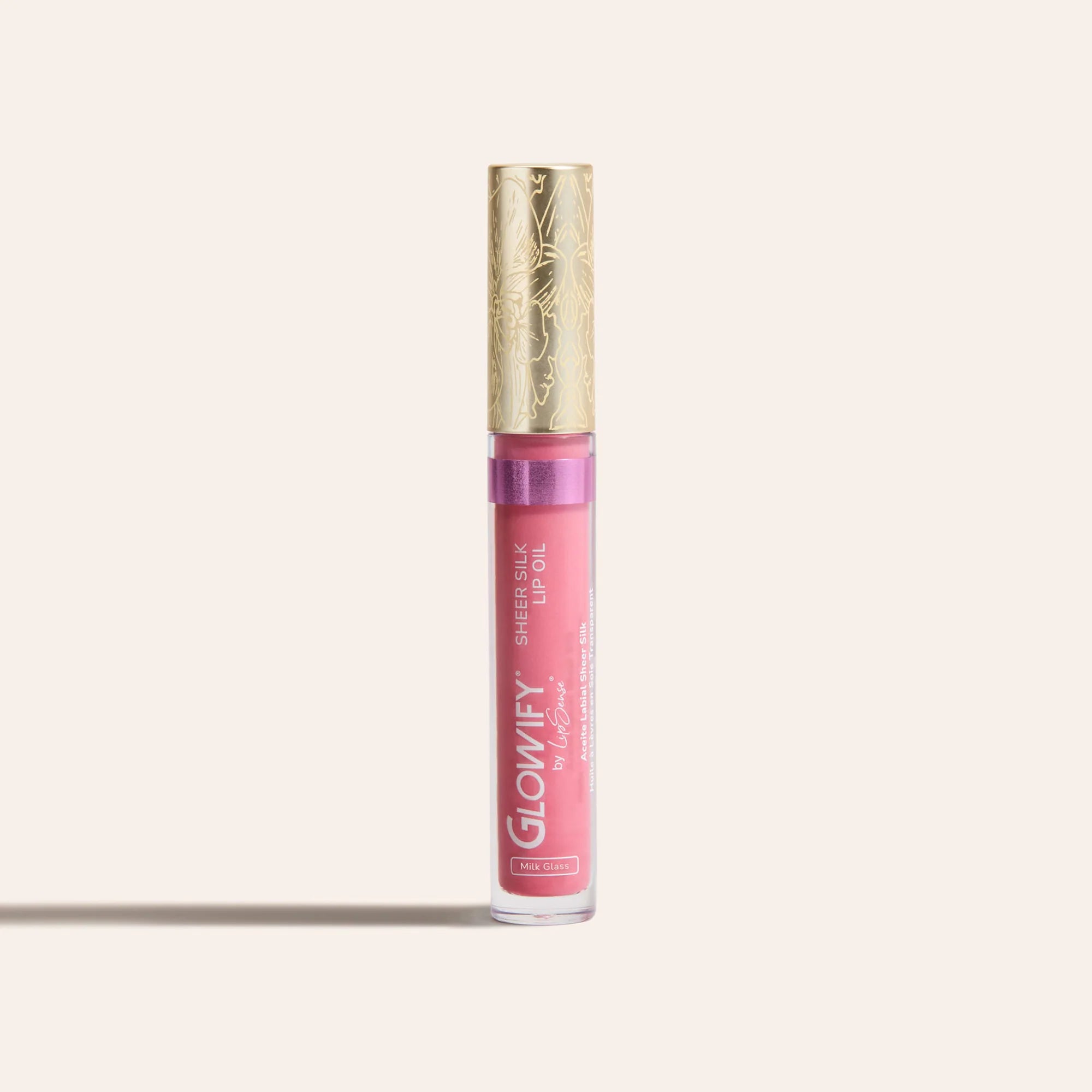 Pink sheer silk lip oil in a clear tube with a gold decorative cap standing upright